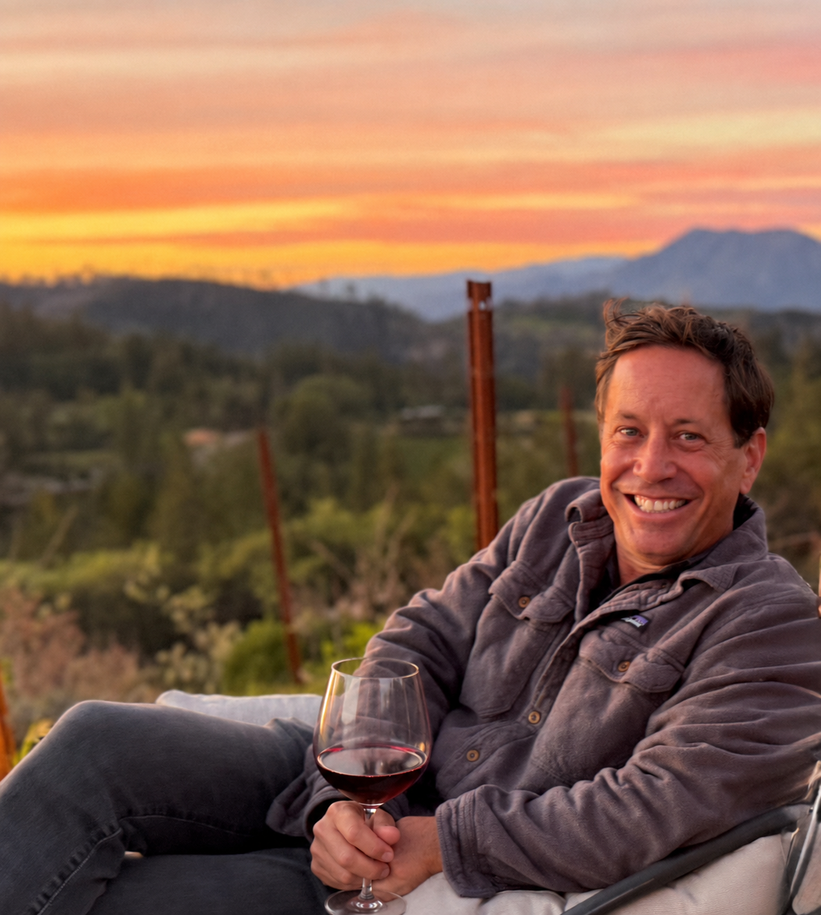 Man enjoying a glass of red wine at sunset in a vineyard setting.